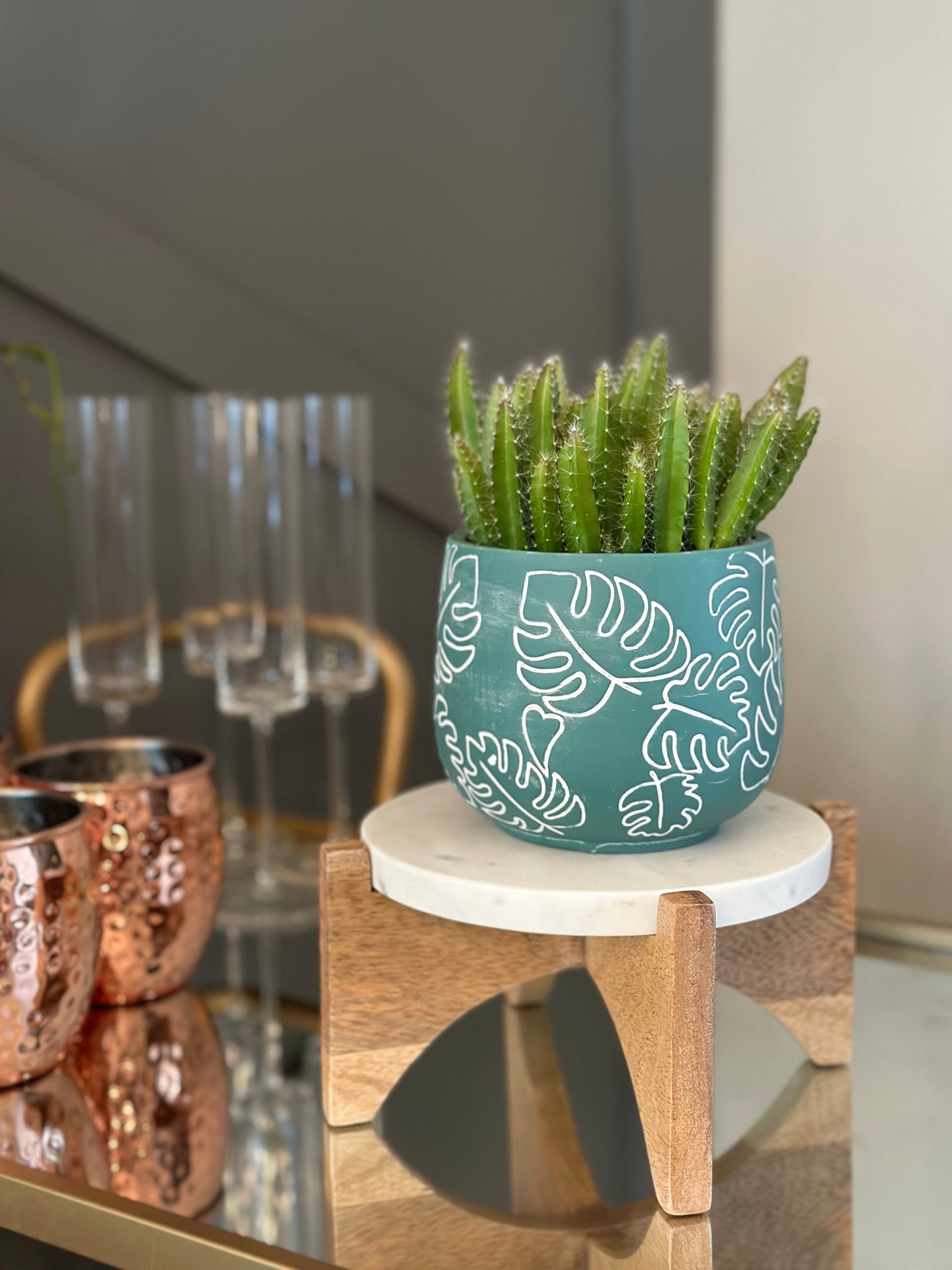 A white marble and acacia wood display stand styled with a small cactus in a teal planter