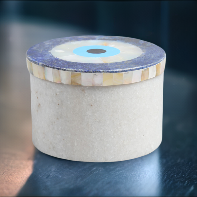 a white lidded marble jar with semi-precious stone evil eye inlay lid, sitting on a dark kitchen counter